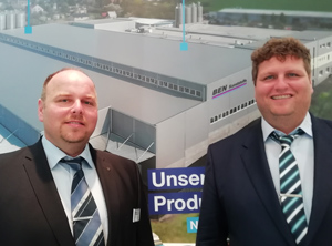 Die Geschäftsführer Rainer und Richard Bühler auf der K 2019 vor einem Foto der erweiterten Produktionsstätte (Foto: KI)